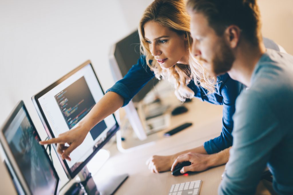 Two people using a computer business simulator with one of them pointing at the screen.