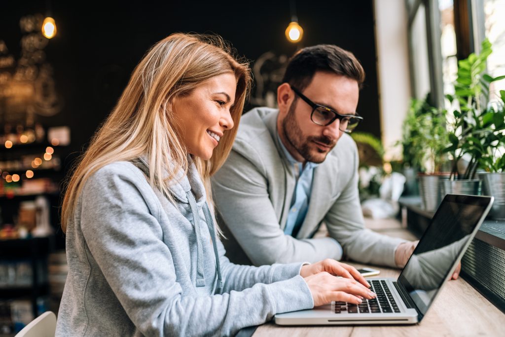 Two business people at a cafe looking at laptop and smiling whilst seeking to develop workplace talent