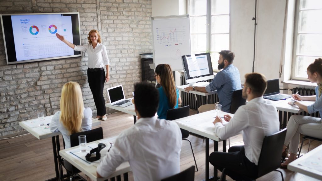 Teacher explaining charts to a room of students and professionals.