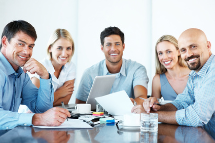 Business people around a table using laptop and smiling.