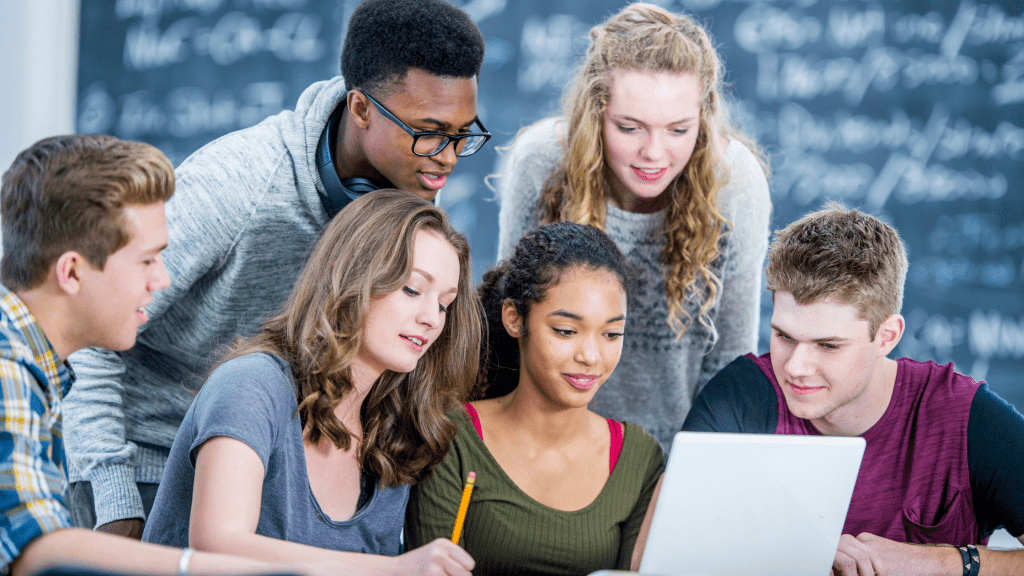 University students engaged and working together around a computer using the business simulation software by SimVenture. This is a digital learning transformation mirroring the real world.